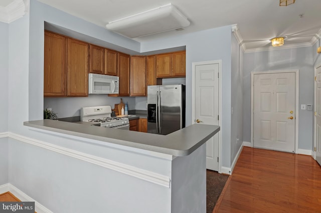 kitchen with a peninsula, white appliances, dark wood-type flooring, ornamental molding, and brown cabinets