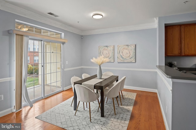 dining area with light wood-style floors, visible vents, crown molding, and baseboards