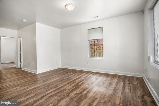 empty room with dark wood-style floors, visible vents, and baseboards