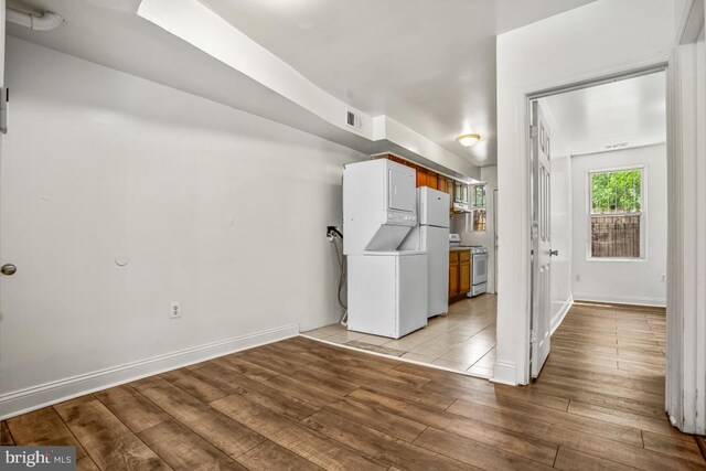 clothes washing area featuring visible vents, light wood-style floors, stacked washer / dryer, laundry area, and baseboards