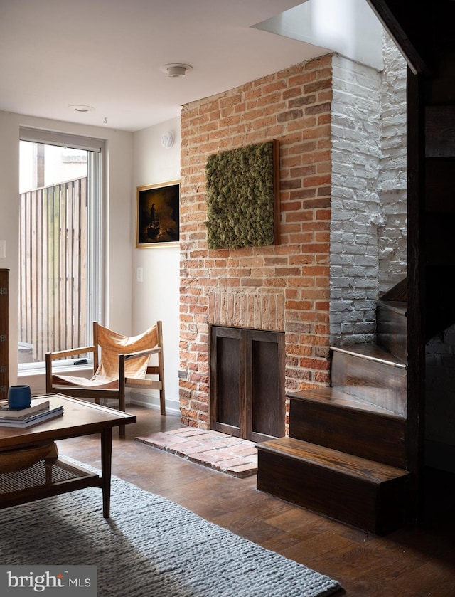 living area with baseboards, a brick fireplace, and wood finished floors