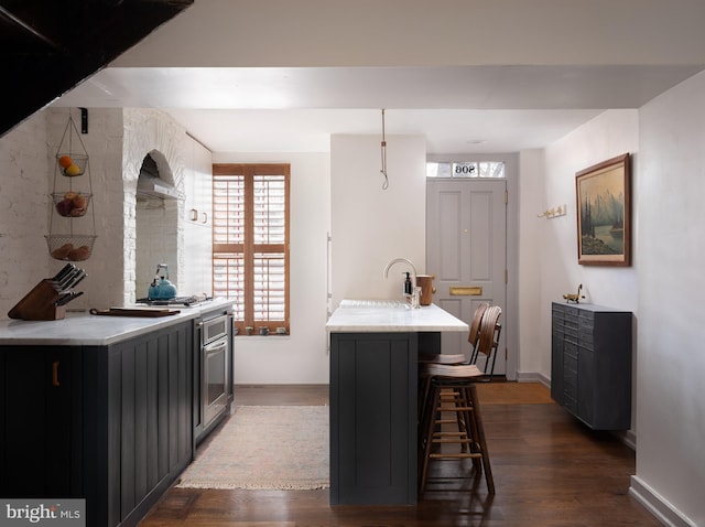 kitchen featuring light countertops, a kitchen breakfast bar, stainless steel gas stove, and dark wood-type flooring