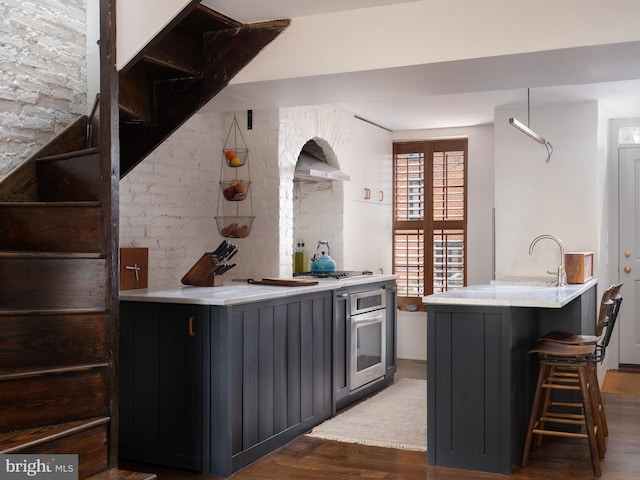 interior space featuring a sink, wood finished floors, stainless steel appliances, wall chimney exhaust hood, and brick wall