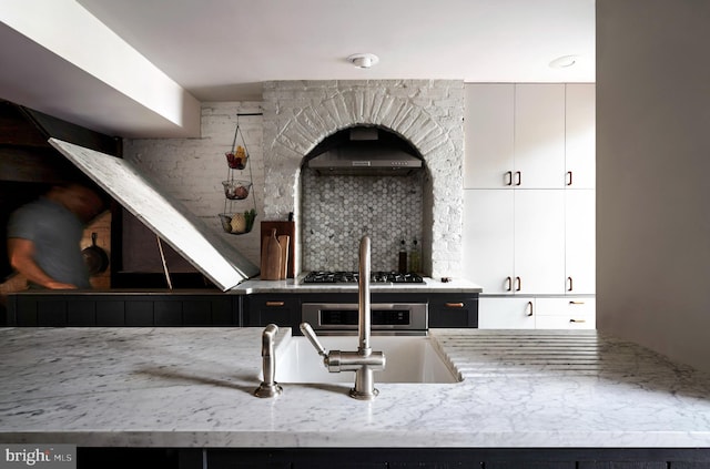 kitchen featuring light stone countertops, decorative backsplash, stainless steel gas stovetop, wall oven, and exhaust hood