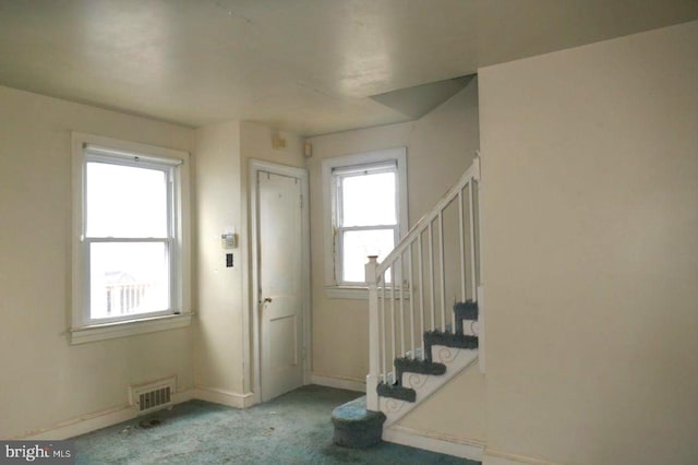 entryway featuring baseboards, stairs, visible vents, and light colored carpet