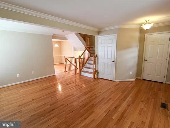 spare room featuring wood finished floors, visible vents, baseboards, ornamental molding, and stairway