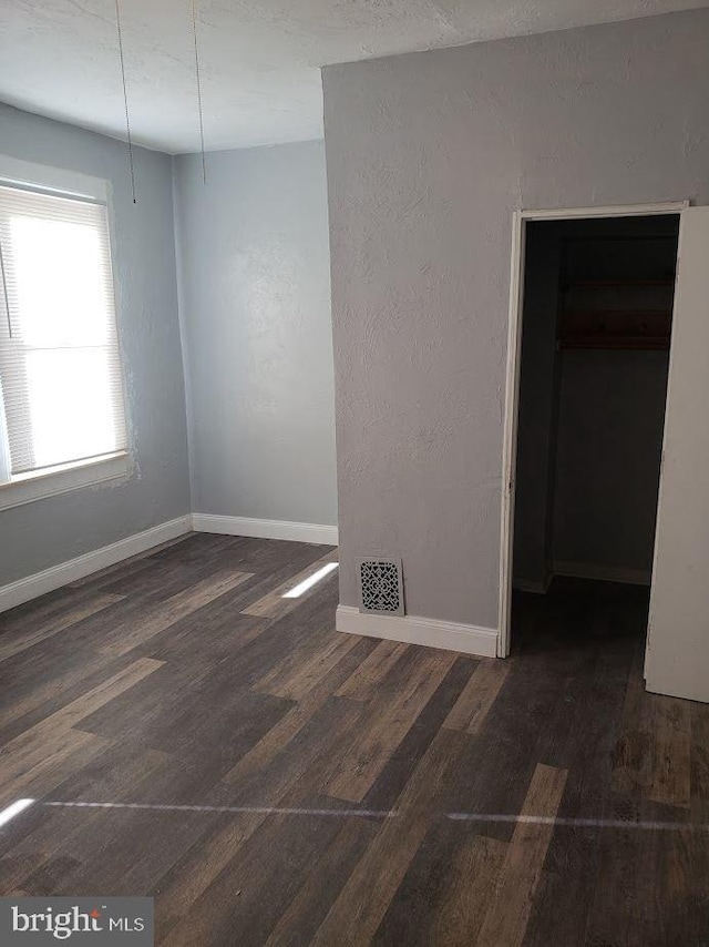 unfurnished room featuring visible vents, a textured wall, baseboards, and wood finished floors