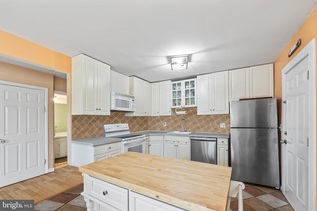 kitchen featuring decorative backsplash, glass insert cabinets, stainless steel appliances, white cabinetry, and a sink