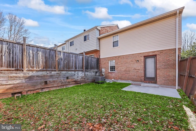 rear view of house with brick siding, a patio, a lawn, central AC unit, and a fenced backyard