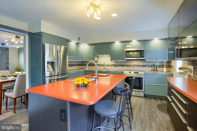 kitchen with stainless steel appliances, tasteful backsplash, modern cabinets, a sink, and wood finished floors