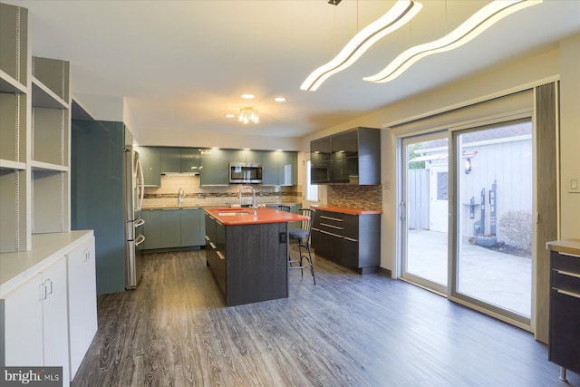 kitchen with a center island with sink, decorative backsplash, appliances with stainless steel finishes, dark wood-style flooring, and a sink