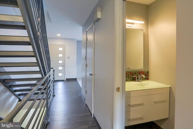 hallway featuring recessed lighting, a sink, baseboards, stairs, and dark wood finished floors