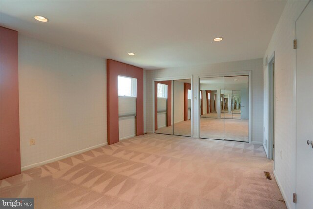 unfurnished bedroom featuring recessed lighting, light colored carpet, visible vents, baseboards, and two closets