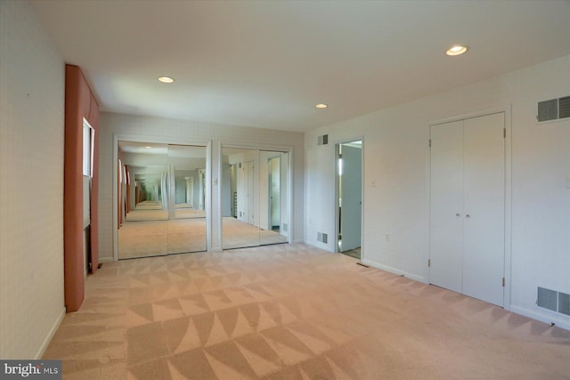 unfurnished bedroom featuring recessed lighting, two closets, visible vents, and light colored carpet