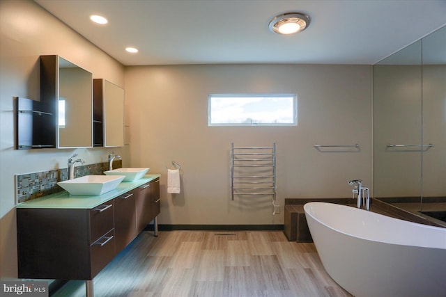 full bath with a freestanding bath, wood finished floors, a sink, and baseboards