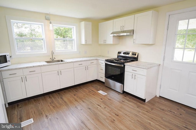 kitchen featuring white microwave, under cabinet range hood, a sink, white cabinets, and stainless steel electric stove