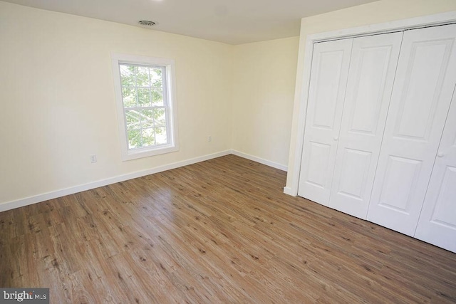 unfurnished bedroom with a closet, visible vents, baseboards, and wood finished floors