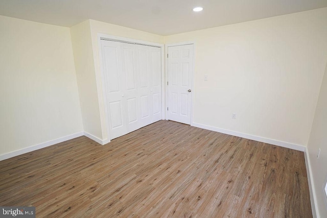 unfurnished bedroom with recessed lighting, a closet, baseboards, and wood finished floors