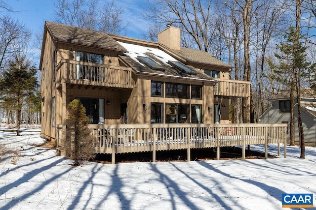 snow covered back of property with a deck, a chimney, a shingled roof, and a balcony