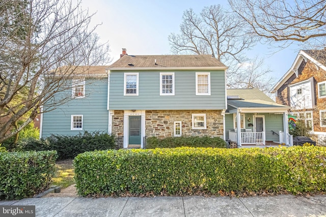 view of front of house with a porch, stone siding, and a chimney