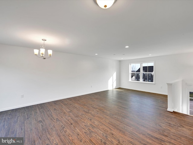 empty room featuring dark wood-style floors, recessed lighting, baseboards, and an inviting chandelier