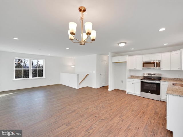 kitchen with open floor plan, wood finished floors, hanging light fixtures, stainless steel appliances, and white cabinetry