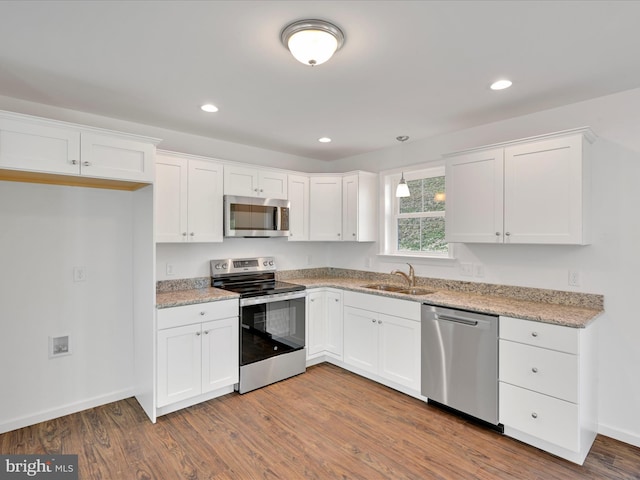 kitchen with stainless steel appliances, wood finished floors, a sink, white cabinets, and pendant lighting