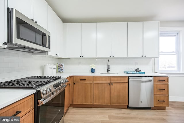 kitchen featuring stainless steel appliances, light countertops, a sink, and white cabinetry