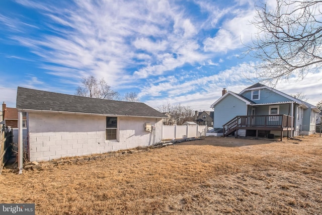 exterior space featuring concrete block siding, roof with shingles, a yard, fence, and a deck