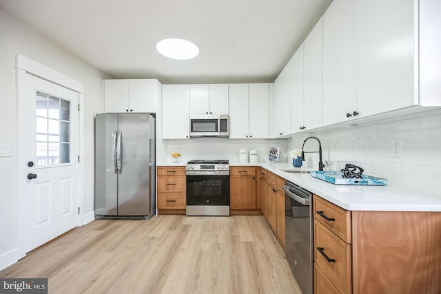 kitchen with stainless steel appliances, light countertops, light wood-style floors, white cabinets, and a sink