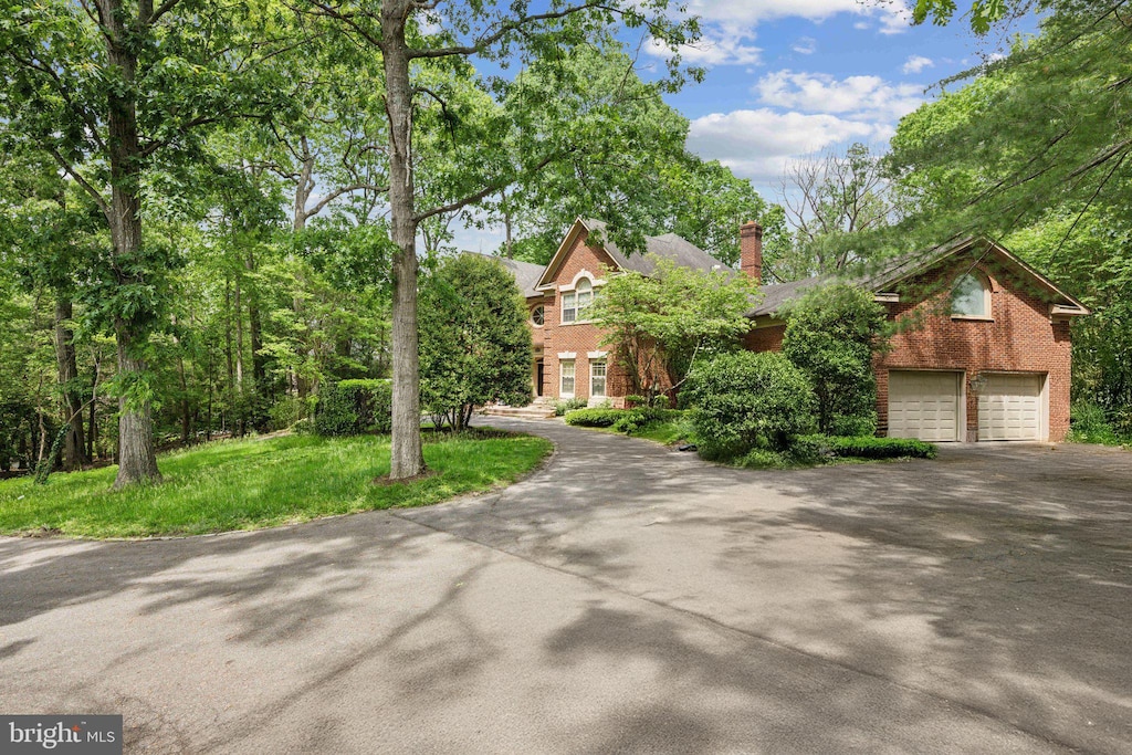 view of front of house featuring brick siding, asphalt driveway, a chimney, and an attached garage