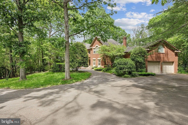 view of front of house featuring brick siding, asphalt driveway, a chimney, and an attached garage