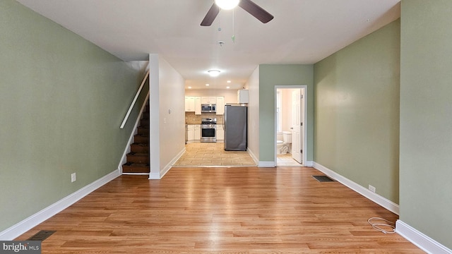 unfurnished living room with a ceiling fan, visible vents, stairs, baseboards, and light wood-type flooring