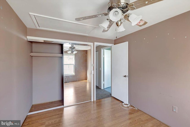 unfurnished bedroom with attic access, wood finished floors, and a ceiling fan