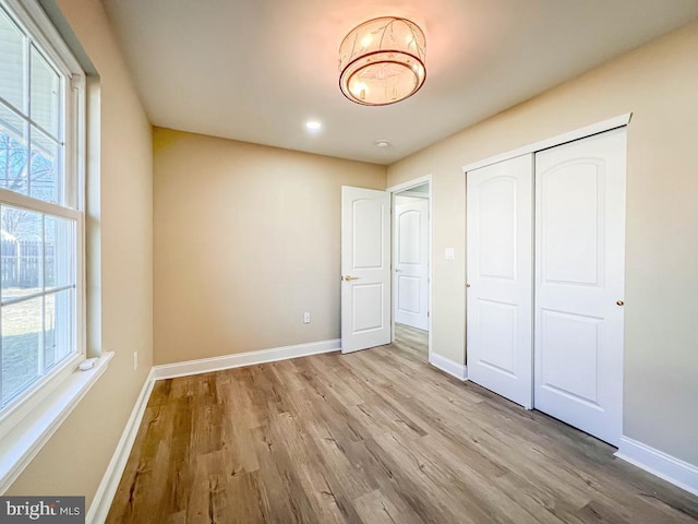 unfurnished bedroom with multiple windows, light wood-style flooring, and baseboards