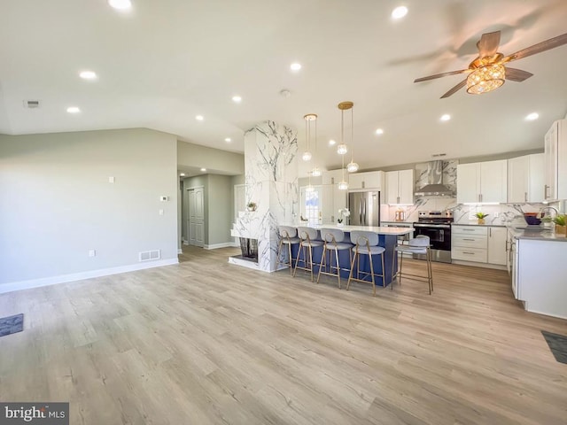 kitchen with white cabinets, hanging light fixtures, stainless steel appliances, light countertops, and wall chimney range hood