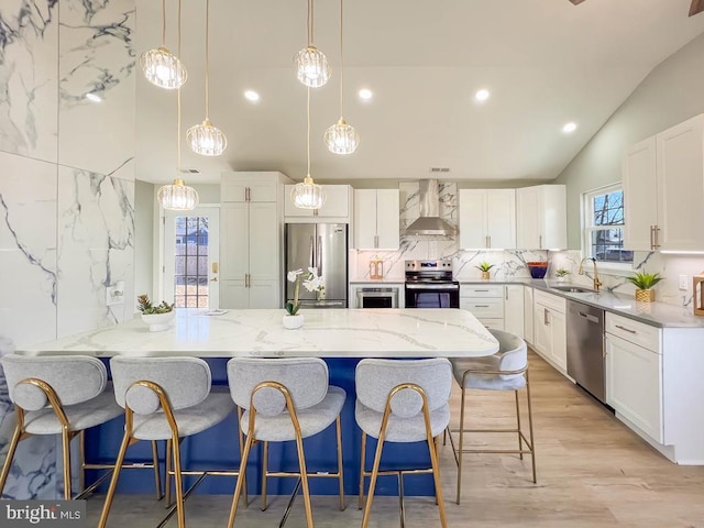 kitchen featuring stainless steel appliances, white cabinetry, hanging light fixtures, and wall chimney range hood