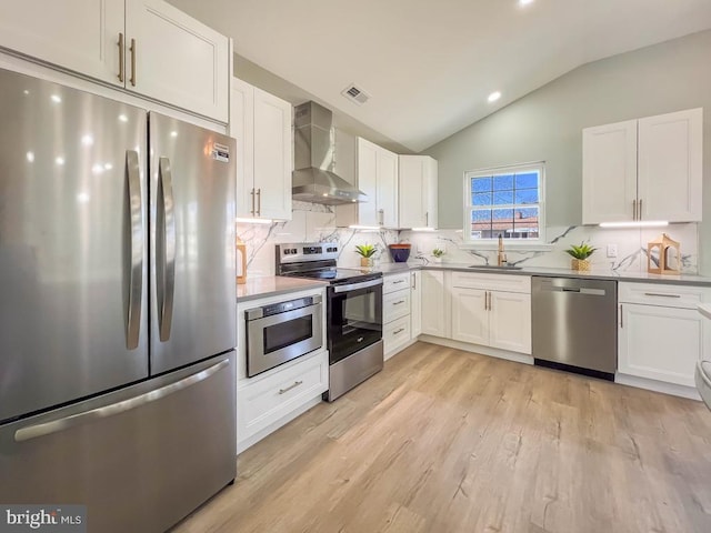 kitchen featuring a sink, appliances with stainless steel finishes, wall chimney range hood, and white cabinetry