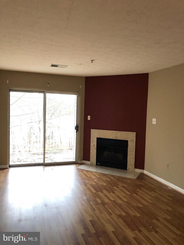 unfurnished living room with baseboards, visible vents, wood finished floors, a textured ceiling, and a high end fireplace