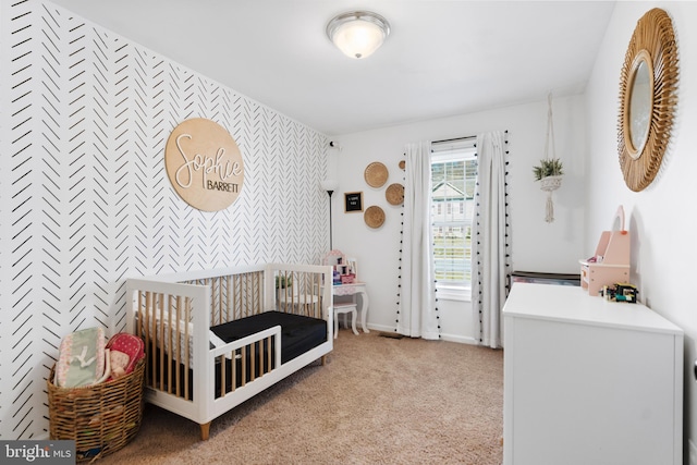 bedroom featuring light colored carpet, an accent wall, baseboards, a nursery area, and wallpapered walls