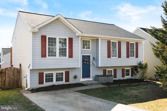 split foyer home featuring fence, a front lawn, and roof with shingles