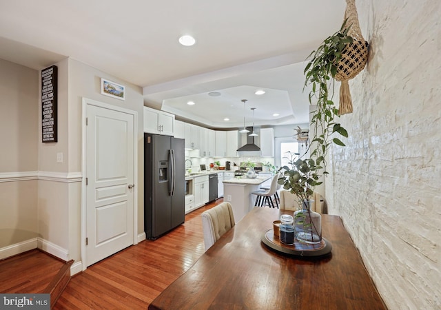 dining area with light wood-style flooring, baseboards, a raised ceiling, and recessed lighting