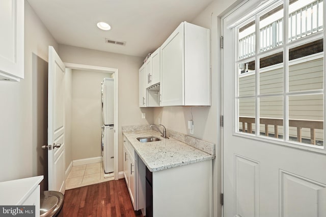 kitchen with light stone counters, stacked washer and dryer, a sink, visible vents, and white cabinetry