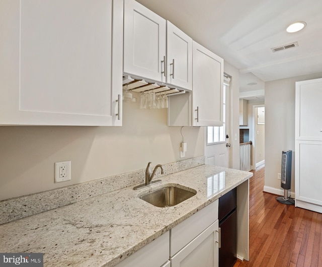 kitchen with light stone counters, visible vents, a sink, and white cabinetry