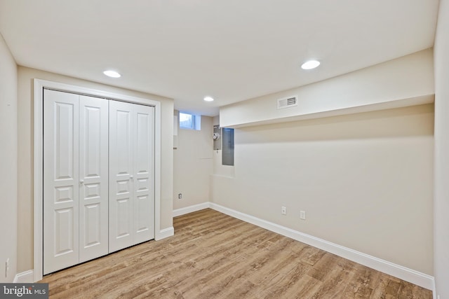 basement featuring light wood-style flooring, electric panel, visible vents, and baseboards