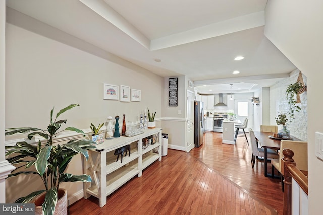 hallway featuring baseboards, a raised ceiling, wood finished floors, and recessed lighting