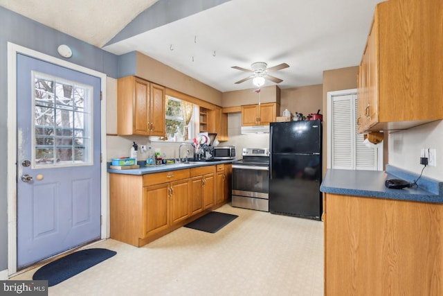 kitchen with light floors, dark countertops, appliances with stainless steel finishes, a sink, and under cabinet range hood