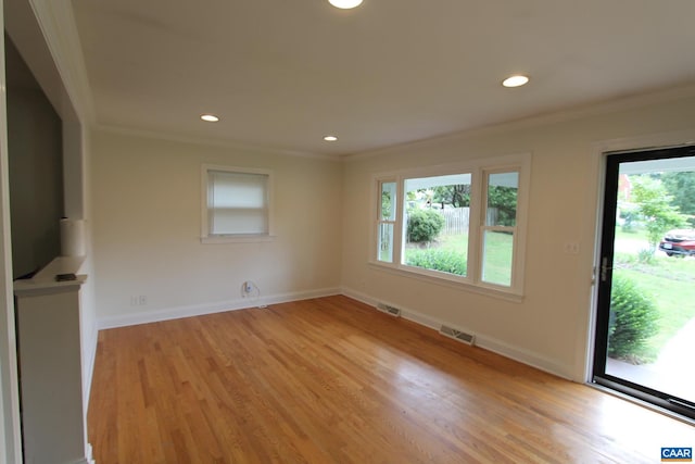 empty room with ornamental molding, light wood-type flooring, visible vents, and baseboards