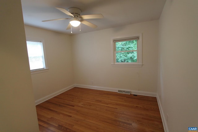 empty room featuring a wealth of natural light, wood finished floors, visible vents, and baseboards