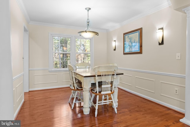 dining room featuring a wainscoted wall, ornamental molding, wood finished floors, and ornate columns